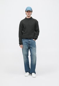 Dunkelgrauer Strickpullover mit hohem Kragen, kombiniert mit hellblauen geraden Jeans und weißen Sneakers. Die Accessoires umfassen eine hellblaue Kappe.