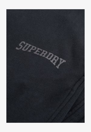 Tissu gris foncé avec une texture lisse affichant le mot "SUPERDRY" en lettres grises claires contrastantes sur toute sa surface.