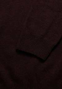 Bordeauxroter Pullover aus weichem, strukturiertem Strick. Verfügt über eine gerippte Manschette mit glatter, gleichmäßiger Oberfläche. Reiche, tiefe Farbe mit minimal sichtbareren Fasern.