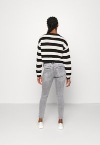 Suéter corto a rayas en blanco y negro, combinado con jeans skinny de tiro alto en gris claro y zapatillas blancas. Tejido de punto texturizado visible.