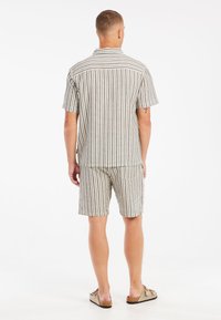 Ensemble composé d'une chemise à manches courtes et d'un short en tissu rayé, avec des couleurs douces, une coupe décontractée et une poche arrière sur le short.