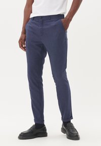Pantalones ajustados azul marino con un acabado texturizado, que cuentan con dos bolsillos laterales y un cierre de botón. Combinados con zapatos negros tipo slip-on.