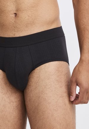 Schwarze Baumwollslips mit geripptem Textur, elastischem Taillenbund und konturiertem Vorderdesign, präsentiert vor einem neutralen Hintergrund.
