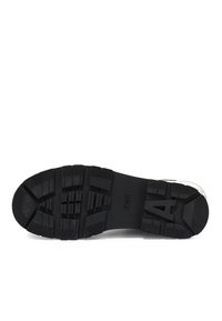 Semelle de chaussure en caoutchouc noir avec une surface texturée, présentant des motifs profonds et une légère courbure au niveau des orteils. Les marquages comprennent "AIRE" et le numéro "4."