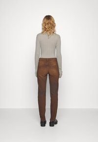 Jeans de mezclilla marrones con parches de un marrón más claro en contraste, diseño de cintura alta y silueta ajustada. Top de manga larga acanalada en gris.