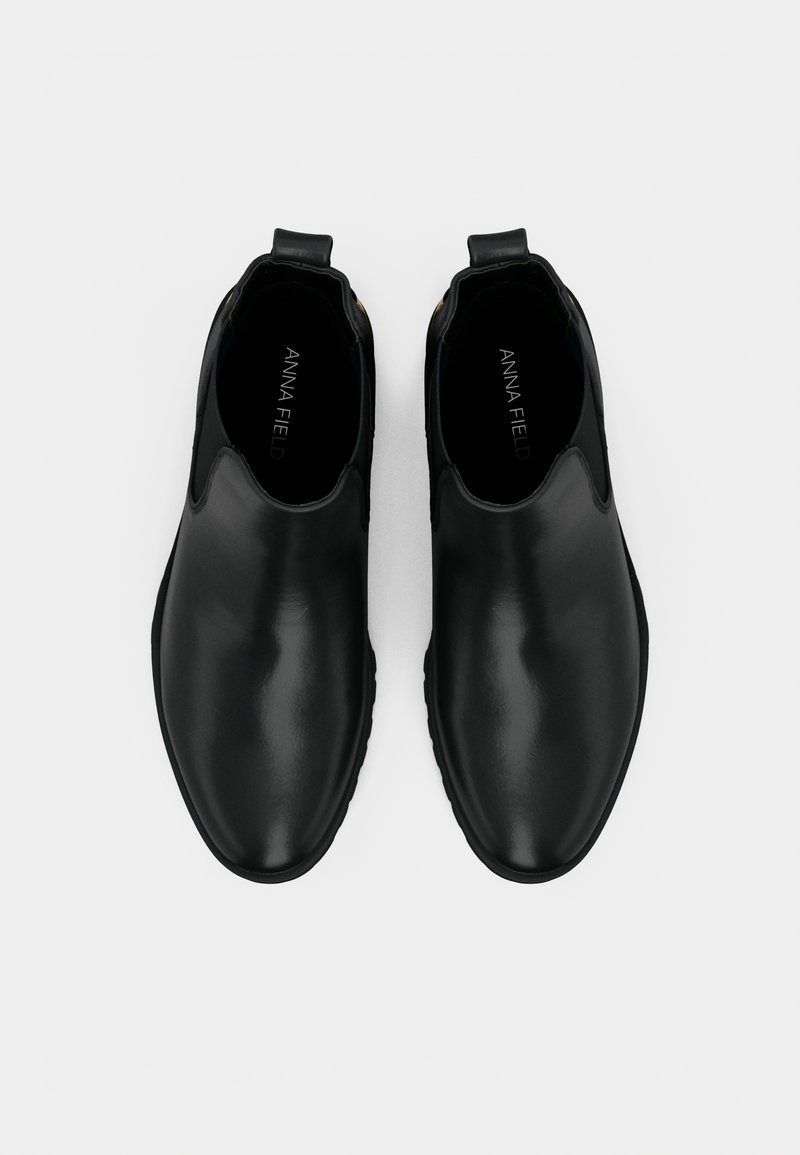 Bottines noires en cuir à enfiler, à bouts ronds et avec des languettes, vues de dessus sur un fond blanc.