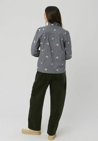 Chemise à carreaux noir et blanc brodée de fleurs avec un dos froncé, associée à un pantalon en velours côtelé vert olive et des chaussures à plateforme beiges.