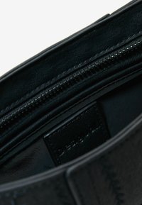 Borsa in pelle nera con una finitura liscia e testurizzata. L'interno presenta una tasca con zip e un'etichetta in tessuto con il marchio.