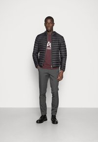 Black puffer jacket with horizontal stitching, maroon T-shirt with white logo, gray slim-fit trousers, and black lace-up boots.