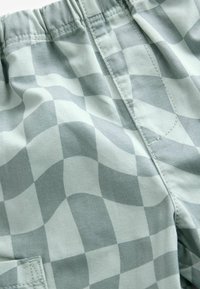 Hellgraue Shorts aus weichem Stoff, mit einem karierten Muster aus überlappenden Quadraten, elastischem Bund und sichtbaren Nähdetails.