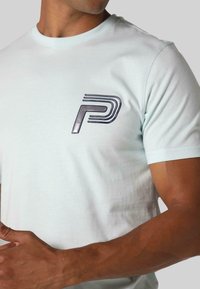 Gaiši zila kokvilnas T-kreklu, ar spīdīgu tumši zilu "P" logotipu un līniju akcentiem kreisajā krūtī. Īsas piedurknes un apaļš kakls.