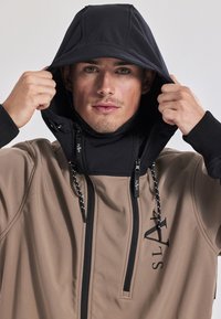Herren zweifarbige Jacke mit schwarzer Kapuze und beigem Oberteil. Verfügt über einen hohen Kragen, einen Frontreißverschluss und verstellbare Kordeln. Glatte Textur.