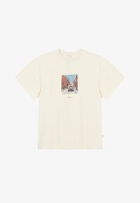 Cremefarbendes Baumwoll-T-Shirt mit einem quadratischen Grafikdesign, das eine illustrierte Straßenansicht zeigt, kurzen Ärmeln und einem lockeren Schnitt.