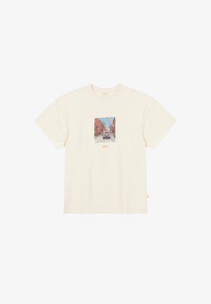 Κρέμα βαμβακερό T-shirt με τετράγωνη γραφική παράσταση που απεικονίζει μια σκηνή από τον δρόμο, κοντά μανίκια και άνετη εφαρμογή.