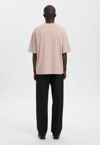 Luźna różowa koszulka z bawełny, krótki rękaw, okrągły dekolt, zestawiona z czarnymi spodniami o szerokich nogawkach. Minimalistyczny design, gładka faktura.