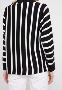 Black and white striped sweater, featuring long sleeves, round neck, and a relaxed fit. Soft fabric with horizontal stripes of varying widths.