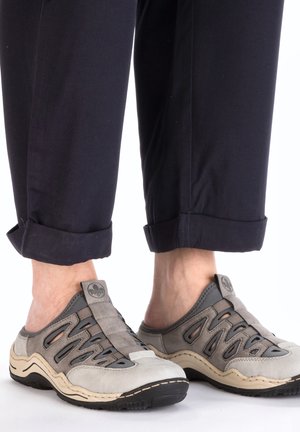 Gray and beige slip-on shoes with a textured upper, openings for ventilation, and a black sole, paired with navy cuffed pants.