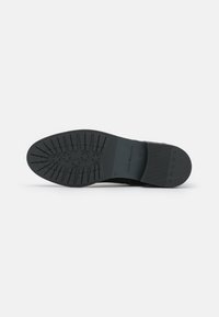 Semelle en caoutchouc noir avec un motif de grip texturé et des accents en étoile. Design robuste avec un profil plat et une section de talon contrastante.
