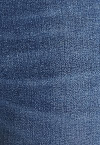 Tela de denim azul oscuro con una textura suave. Presenta un tejido de espiga diagonal y ligeros patrones de desvanecimiento para variar.