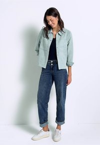 Světle tyrkysová semišová bunda s dvěma předními kapsami, nošená přes černý top. Vytvořeno s ohrnutými modrými džíny a bílými teniskami.