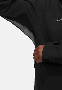 Svart vattentät jacka med dragkedja framtill, justerbara ärmar och en sidficka med dragkedja. Slät utsida med mjukt innerfoder.