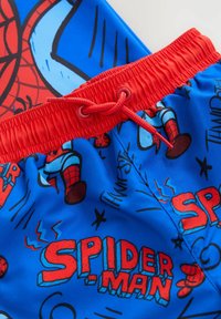 Siniset uimapuvut, joissa on punainen joustava vyötärö ja kiristysnaru. Muotokuvina on Spider-Man-graphicsia ja tekstiä punaisella ja mustalla sinistä taustaa vasten.