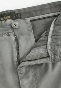 Pantalones grises con cierre de cremallera y botón, fabricados con tejido duradero, costuras cosidas y una textura suave. La etiqueta dice "NEXT Durable Goods."