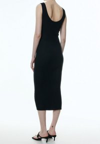 Svart ribbad midiklänning med en figurnära silhuett, rundad rygg och axelband. Bärs med svarta sandaler med remmar.