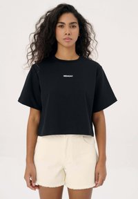 Zwarte crop top met korte mouwen en een wit "MISAGA®" logo op de borst, gecombineerd met off-white versleten shorts.