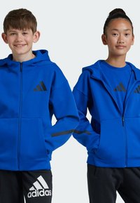 Blå zip-up hoodies med svarta adidas-logotypdetaljer, med fickor och kontrasterande svarta ränder på ärmarna, som är skapade med svarta sweatpants.