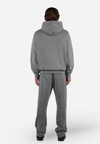 Sudadera gris con capucha grande, puños de canalé y pantalones de chándal grises a juego. El material parece suave; ajuste relajado con un diseño minimalista.
