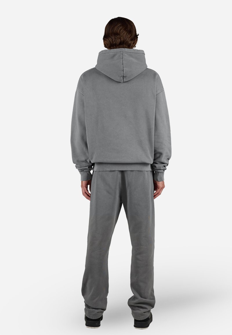 Sudadera gris con capucha grande, puños de canalé y pantalones de chándal grises a juego. El material parece suave; ajuste relajado con un diseño minimalista.