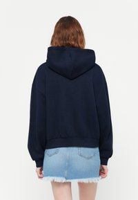 Marineblå avkortet hettegenser med hette, store ermer og ferdig kant, sammen med en lys blå utslitt denimskjørt.