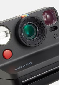 Polaroid camera with black plastic body, green lens, red button, LED flash, and a colorful accent strip on top. Includes "i-Type film" label.