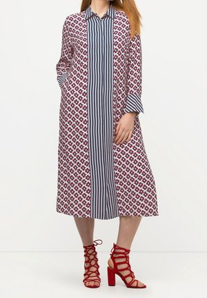 Maxi-jurk met een rood bloemenpatroon op een wit en marineblauw gestreept paneel, lange mouwen, kraaghalslijn en zijzakken, gecombineerd met rode sandalen met bandjes.