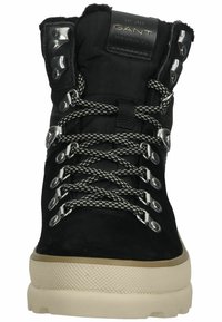 Botín negro de ante hasta el tobillo con ojales de metal, cordones grises y suela de goma color crema. Cuenta con un cuello acolchado y un logo en relieve en la lengüeta.