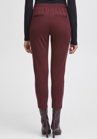 Maroon stretch pants with a relaxed fit, tapered legs, and an elastic waistband. Features two rear pockets and smooth fabric texture.