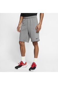 Grijze sportshorts met een elastische tailleband en een zwart Nike-logo. Gecombineerd met rode en zwarte sneakers en witte sokken met gele accenten.