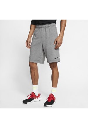 Grijze sportshorts met een elastische tailleband en een zwart Nike-logo. Gecombineerd met rode en zwarte sneakers en witte sokken met gele accenten.