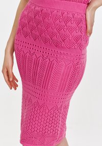 Dzianinowa spódnica ołówkowa w jaskrawym różu, z misternymi wzorami i teksturami, prążkowanym pasem w talii oraz długości do połowy łydki.