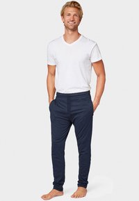 T-shirt blanc à col en V et jogging en tissu doux bleu marine avec poches latérales, design fuselé et taille élastique, porté pieds nus.