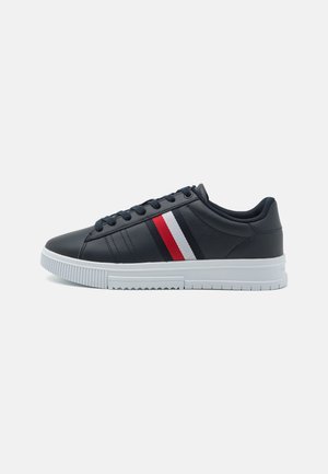 Sneakers sintetici blu navy con suola bianca e texture in rilievo. Presentano strisce rosse e bianche sul lato e dettagli di cucitura tonale.
