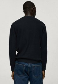 Granatowy sweter z okrągłym dekoltem, ściągaczami na mankietach i u dołu, w połączeniu z niebieskimi dżinsami z tylnymi kieszeniami, wykonanymi z teksturowanego materiału.