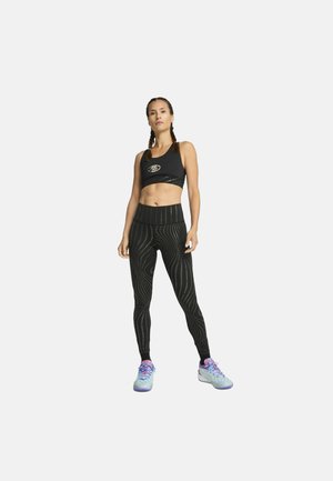 Zwart sportief crop top met een logo, gecombineerd met high-waisted leggings met een golvende lijnpatroon, afgemaakt met lichtblauwe hardloopschoenen.