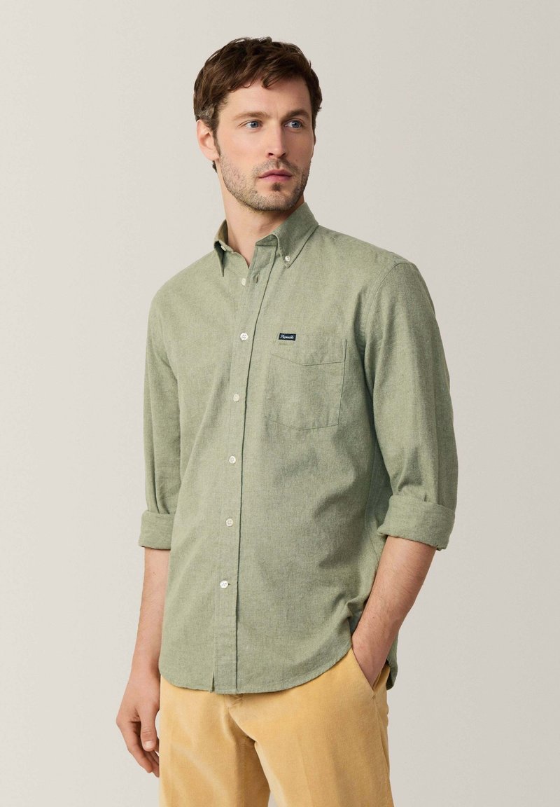 Camisa verde de botones con un bolsillo en el pecho y mangas arremangadas. Hecha de una tela texturada, con una pequeña etiqueta de marca cerca del bolsillo.