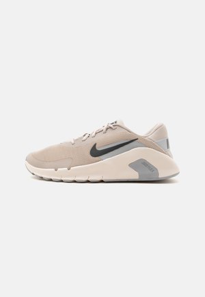 Chaussure de course Nike beige clair avec un swoosh noir, une semelle blanche rembourrée et un patch gris au talon marqué Nike Flex, vue de profil.