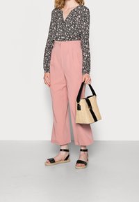 Blouse noire à fleurs, pantalon taille haute rose, sandales espadrilles noires et sac en paille beige avec des accents noirs.