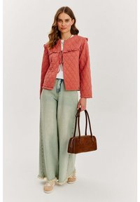 Kurtka w kolorze koralowym, pikowana, z falbaniastym kołnierzem, w połączeniu z jasnoniebieskimi spodniami w szerokim kroju. Brązowa skórzana torebka i beżowe sneakersy dopełniają stylizację.