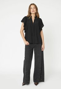 Top nero a maniche corte con dettagli arricciati e collo legato. Abbinato a jeans neri a gamba larga con dettagli in eyelet argentati.