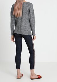 Maglione grigio a maglia con orlo arrotondato e spalle scese, abbinato a jeans skinny in denim scuro con strisce laterali e sandali rossi.